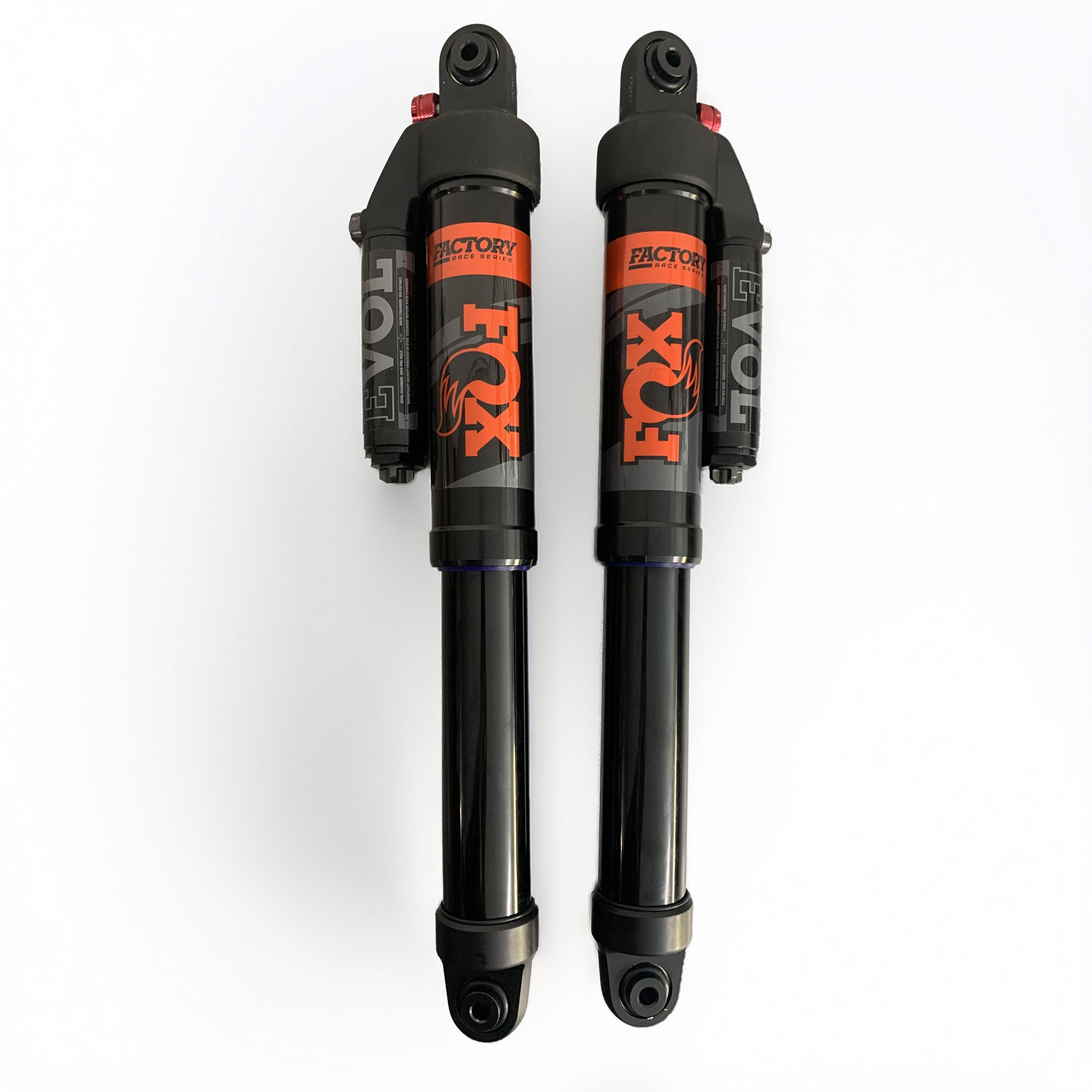 Two Fox Factory shock absorbers side by side on a clean white background, featuring a black body with a prominent orange and black Fox logo and 'Factory' text.